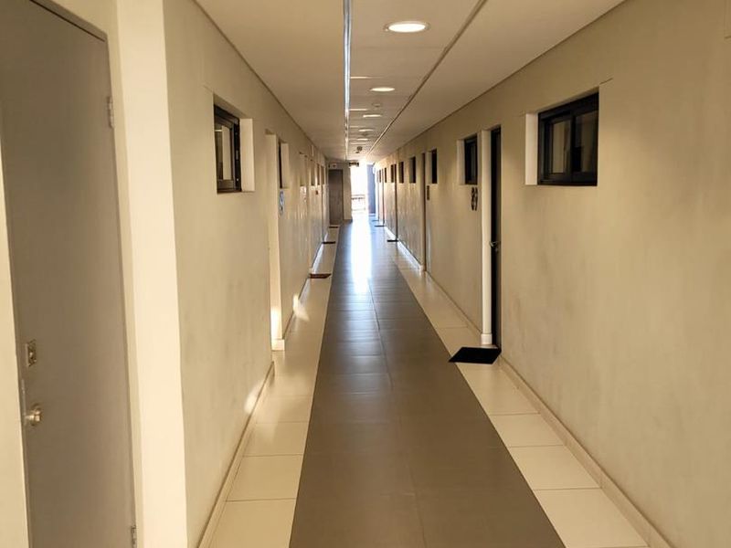 A clean, well-lit apartment building hallway featuring tiled flooring and recessed ceiling lights.