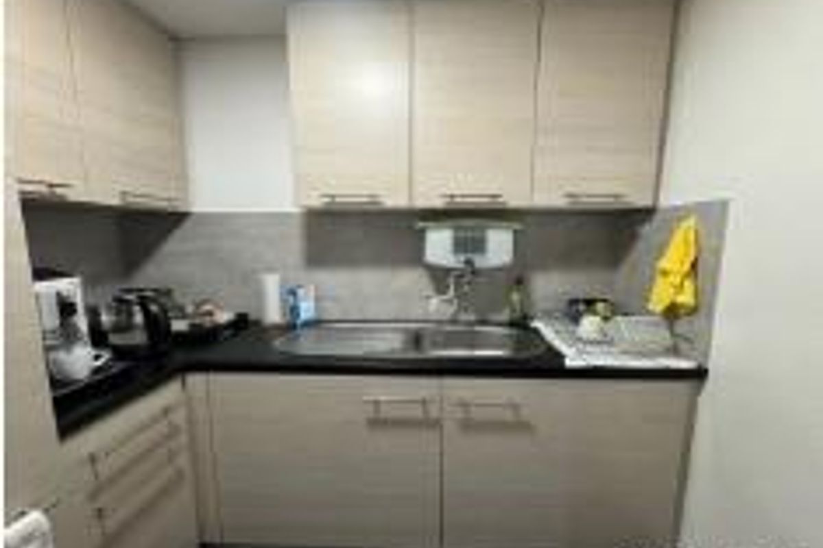 A compact office kitchenette featuring light wood-tone cabinetry, a stainless steel sink, and a tiled backsplash.