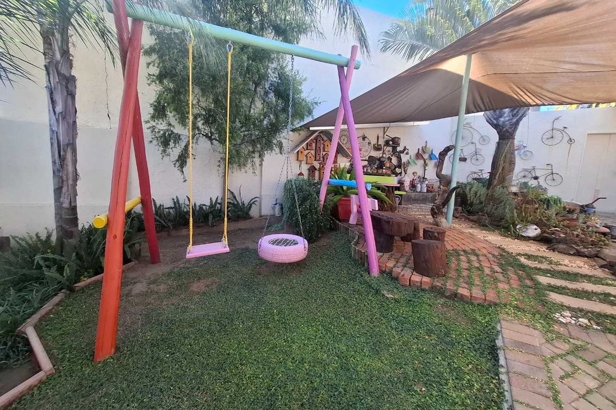 A landscaped rear garden area featuring a shaded patio section, paved pathways, and a dedicated play area with a swing set.
