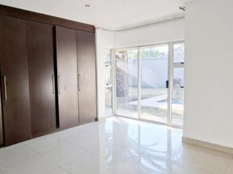 A bright, empty bedroom featuring large built-in cupboards, polished tiled flooring, and a sliding glass door providing direct access to the garden area.
