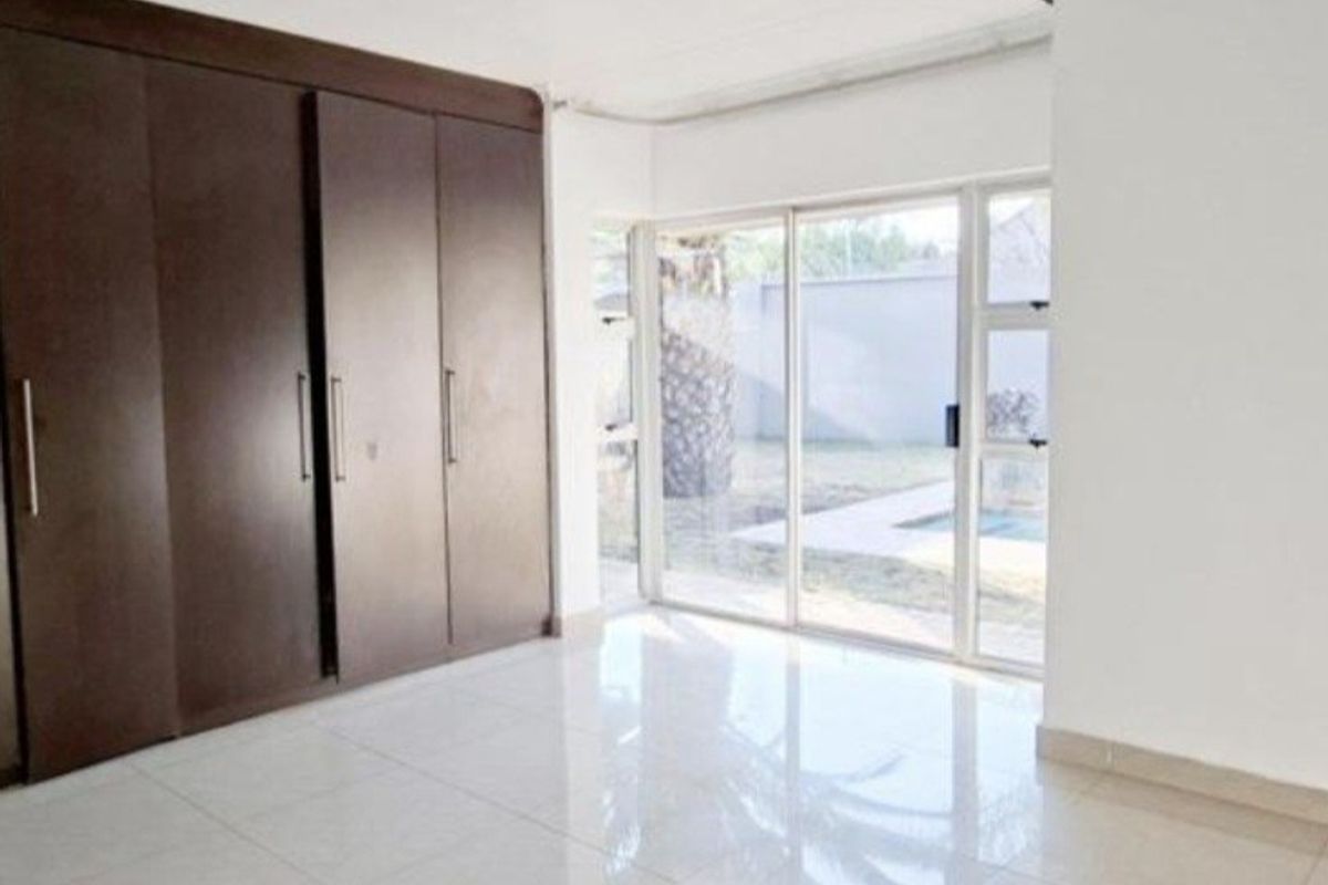 A bright, empty bedroom featuring large built-in cupboards, polished tiled flooring, and a sliding glass door providing direct access to the garden area.