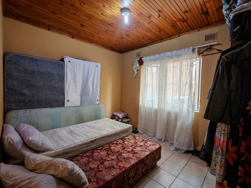 A bedroom featuring a timber tongue and groove ceiling, ceramic tiled flooring, and a window fitted with security bars.