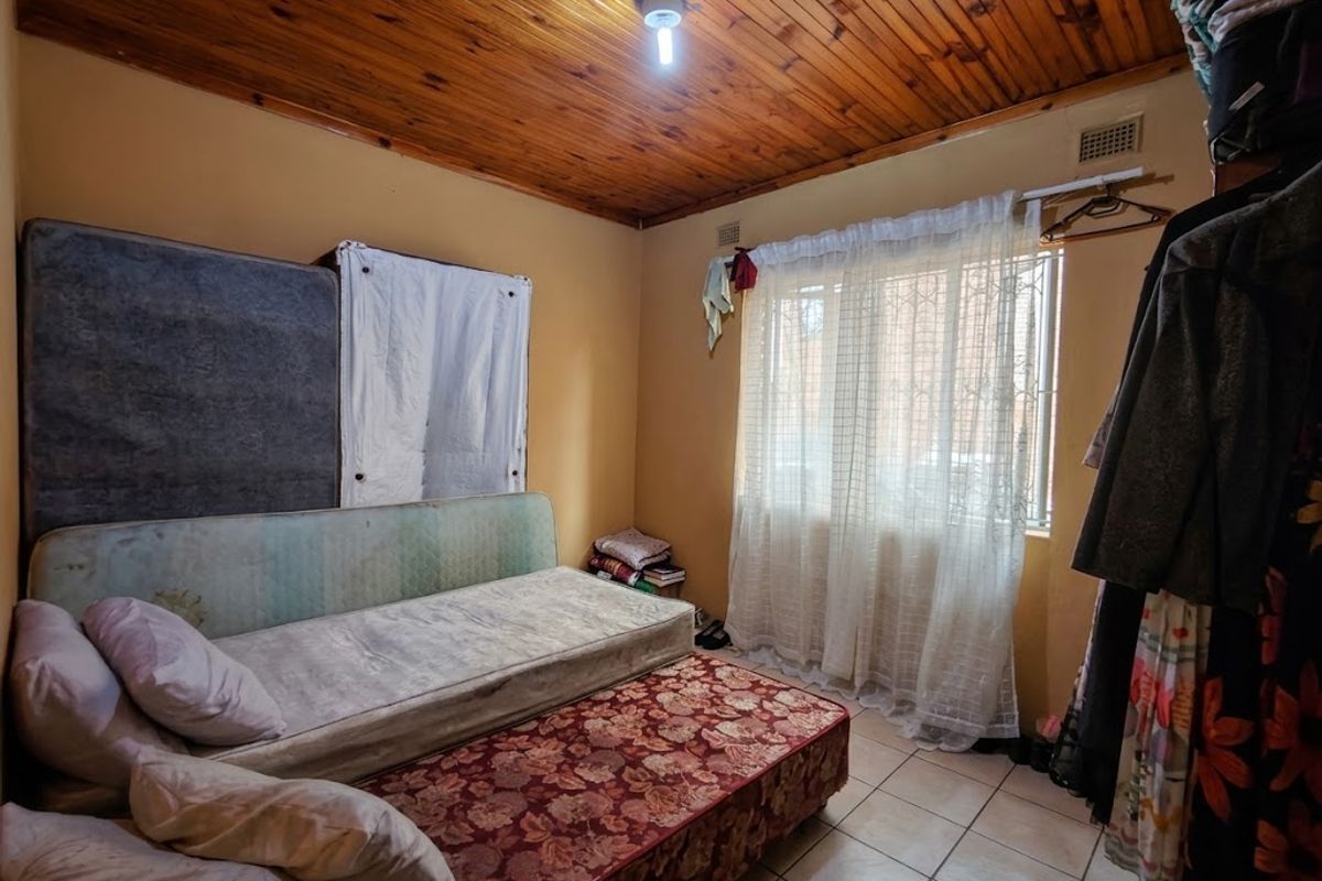 A bedroom featuring a timber tongue and groove ceiling, ceramic tiled flooring, and a window fitted with security bars.
