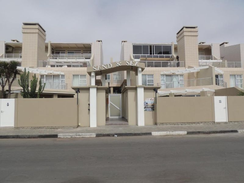 Front elevation of the Sand & Sea penthouse complex, featuring a gated entrance, perimeter walls, and multiple levels with balconies.