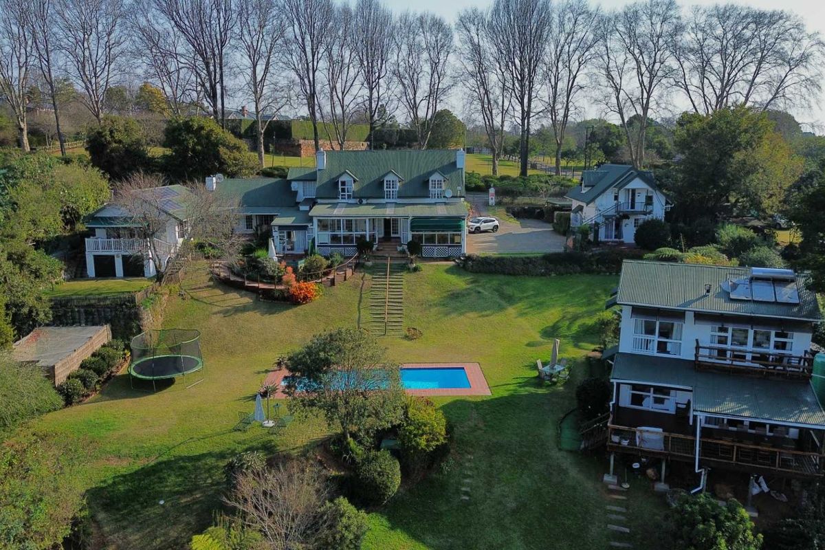 Aerial view of a sprawling property featuring multiple buildings, a swimming pool, landscaped gardens, and extensive timber decking.