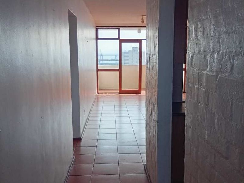 A vacant hallway featuring tiled flooring and a textured brick wall, leading towards a glass door with access to an outdoor balcony area.