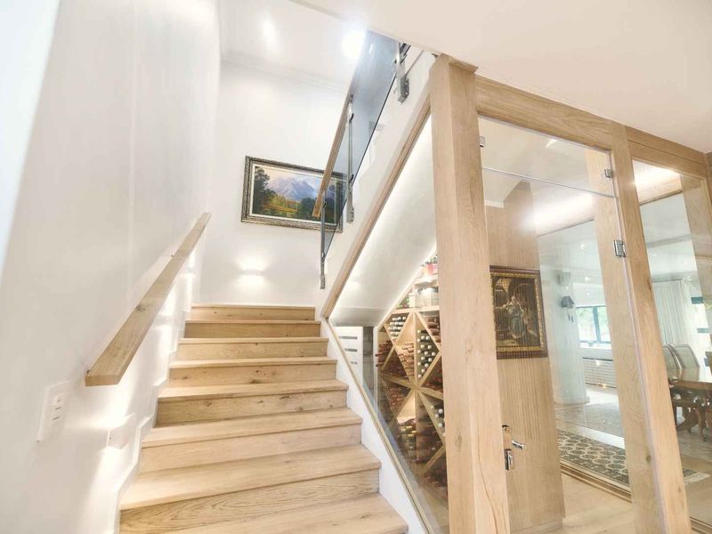 Modern hallway featuring a timber staircase with glass balustrade and an integrated glass-enclosed wine cellar with custom racking.