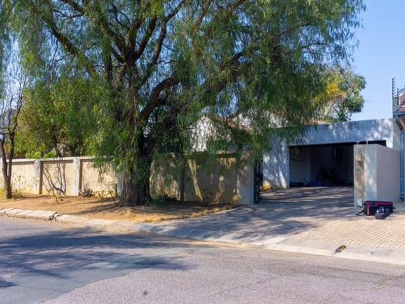 Front view of the property featuring a paved driveway, double garage, and perimeter wall with electric fencing.