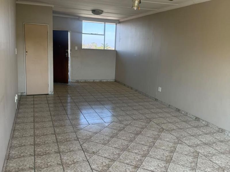 An empty, open-plan living area featuring tiled flooring, a ceiling fan, and neutral wall finishes, offering a blank canvas for interior design.