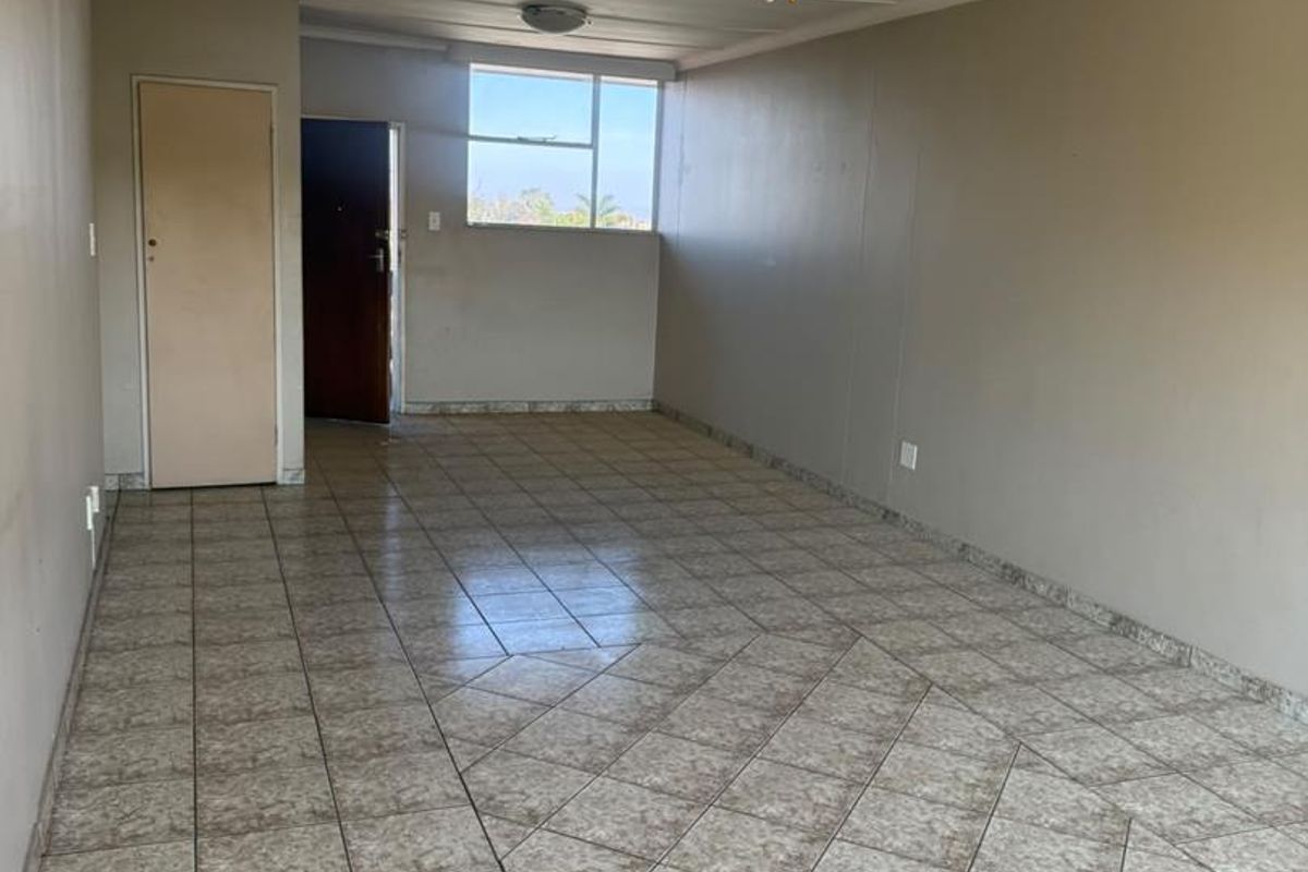 An empty, open-plan living area featuring tiled flooring, a ceiling fan, and neutral wall finishes, offering a blank canvas for interior design.