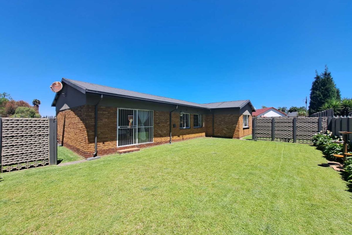 A well-maintained rear exterior view of a face brick house featuring a spacious lawn, secure sliding door access, and perimeter precast concrete walling.
