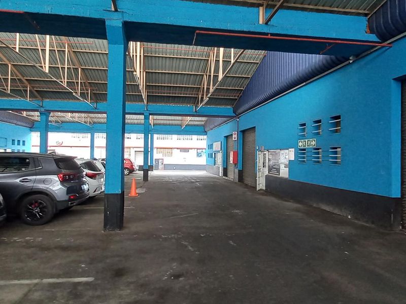 Spacious industrial garage area featuring high steel roof structure, concrete flooring, and multiple roller shutter doors for vehicle access.