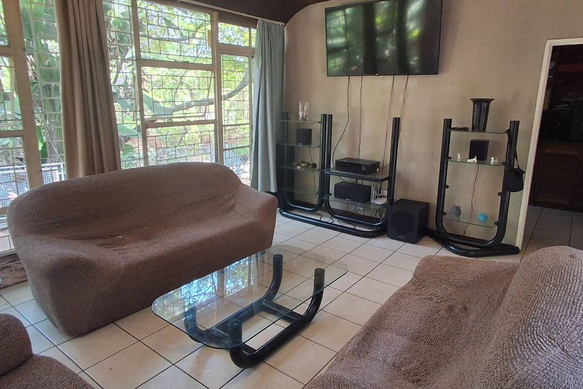 A spacious living room featuring large windows with security bars, tiled flooring, and a wall-mounted television setup.