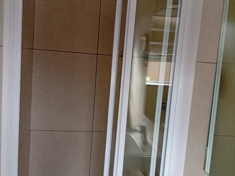 A clean bathroom featuring a modern shower enclosure with tiled walls, a basin with a chrome faucet, and a wall-mounted mirror.