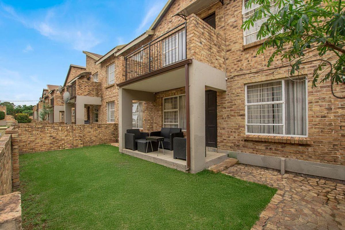 A rear view of the townhouse featuring a covered patio, a small private garden with lawn, and a balcony on the upper level.
