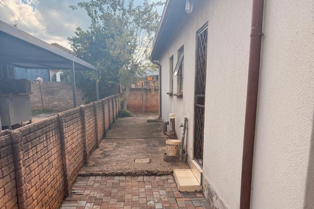 Side exterior view of the property featuring a paved walkway, brick boundary wall, and a metal security gate entrance.