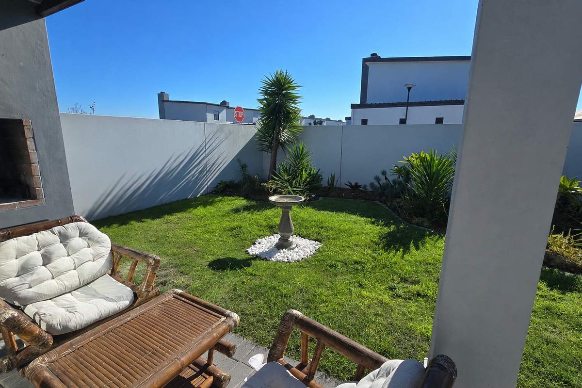 A private rear garden featuring a paved patio area with a built-in braai, well-maintained lawn, and perimeter boundary walls.