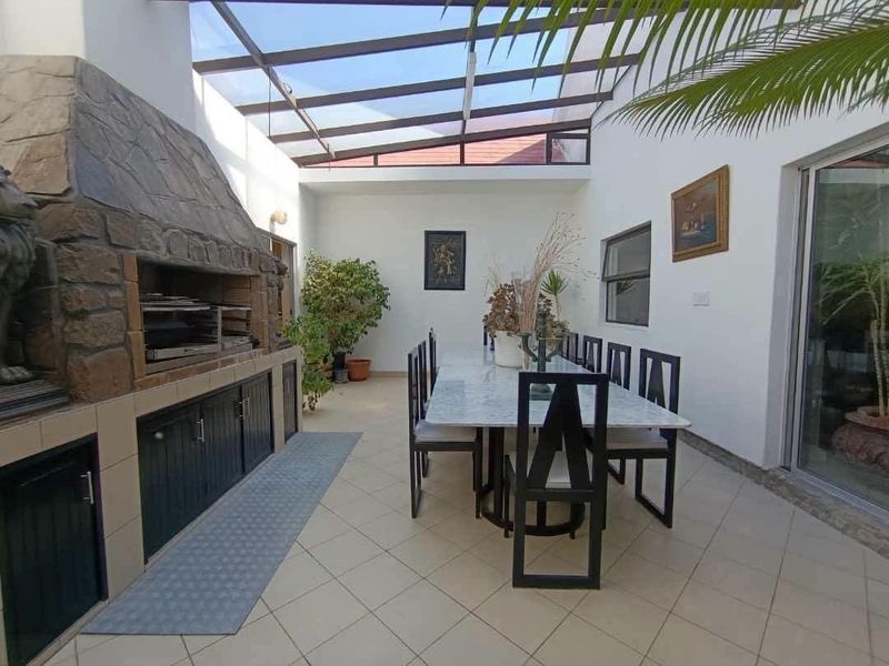 Covered patio area featuring a built-in stone-clad braai, tiled flooring, and a glass roof, providing a bright and functional outdoor entertainment space.