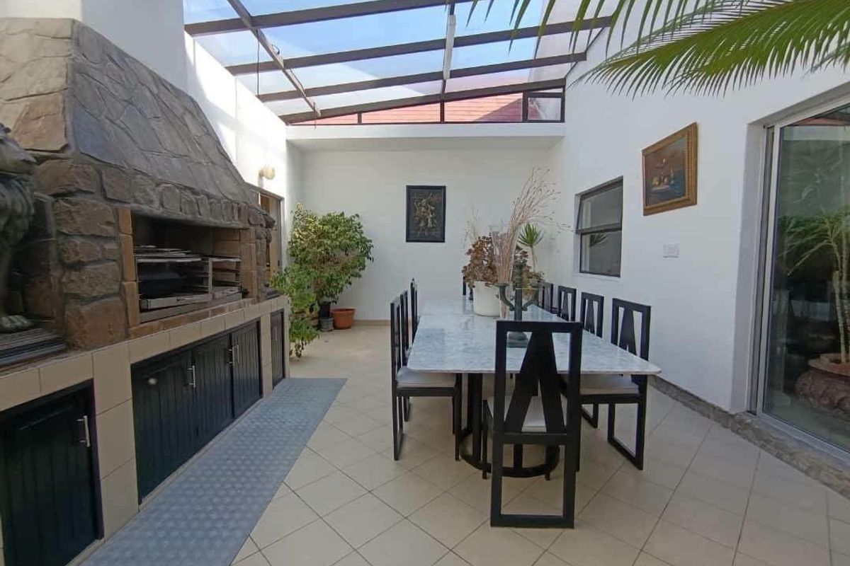 Covered patio area featuring a built-in stone-clad braai, tiled flooring, and a glass roof, providing a bright and functional outdoor entertainment space.