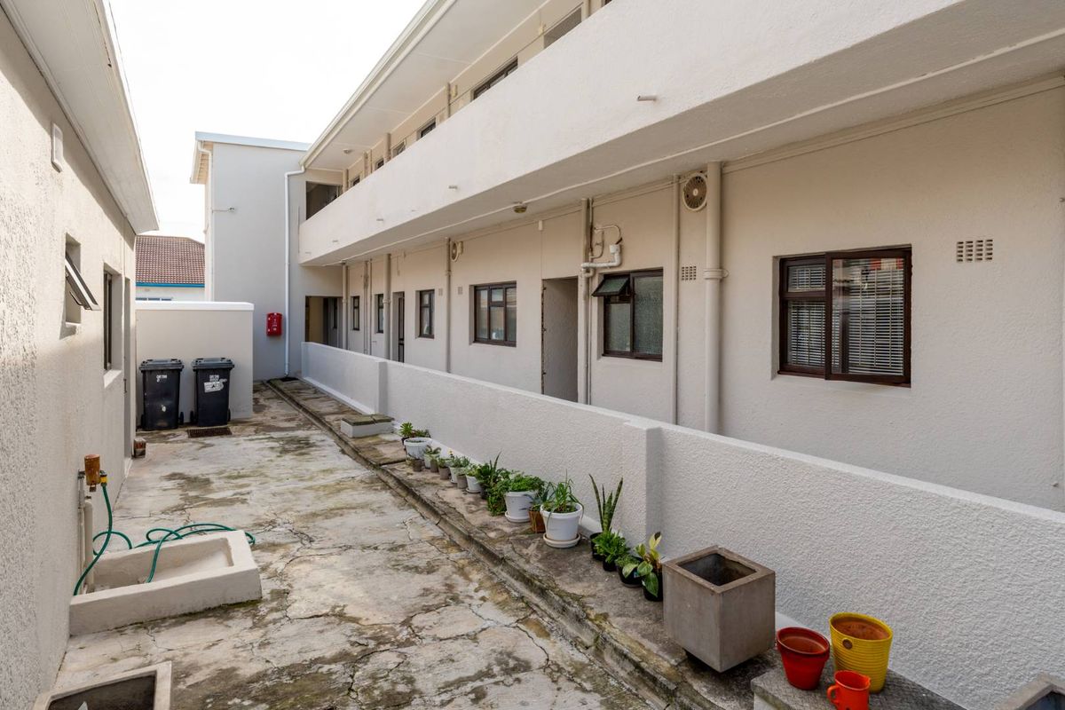 Exterior view of the apartment complex walkway featuring concrete flooring, external wall-mounted plumbing, and access to individual unit entrances.