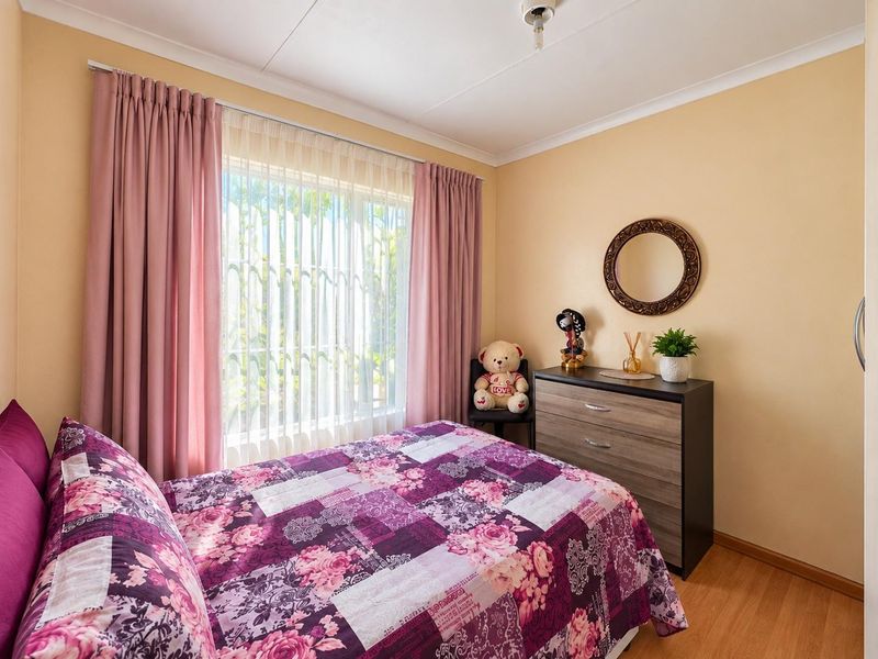 A well-lit bedroom featuring laminate flooring, coved ceilings, and a window fitted with security bars, providing a functional and comfortable living space.