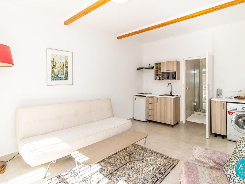 Open-plan living area featuring a kitchenette with built-in cabinetry, sink, and extractor fan, complemented by exposed timber ceiling beams and tiled flooring.