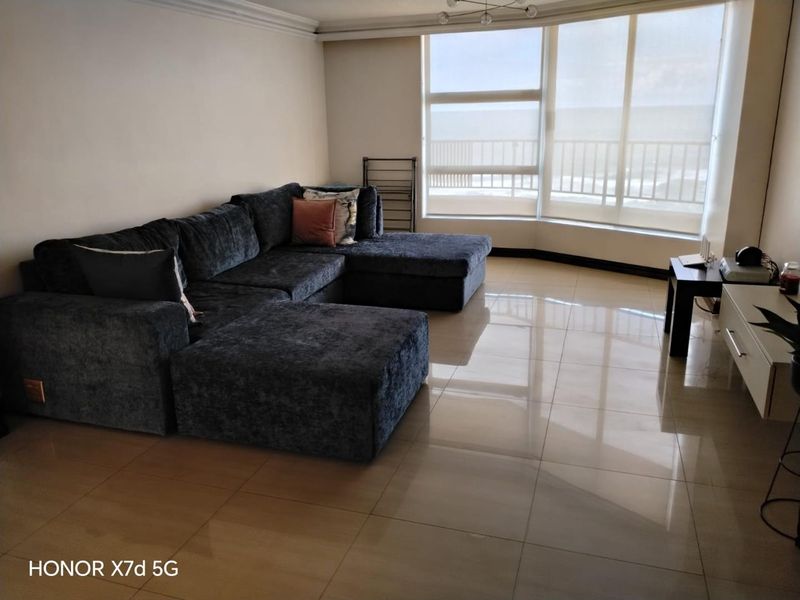 Spacious living room featuring large format floor tiles, ceiling cornicing, and a large bay window with ocean views.
