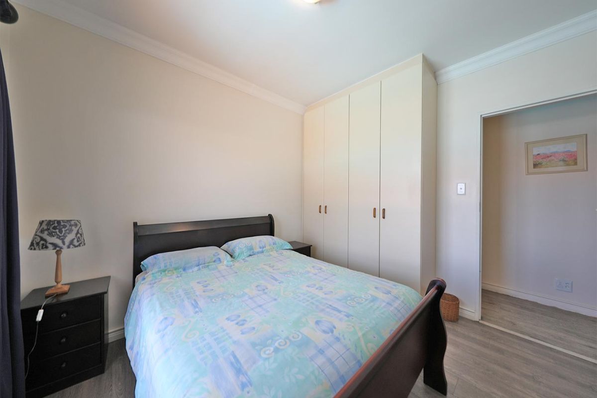 A well-maintained bedroom featuring built-in cupboards, neutral wall finishes, and modern wood-look flooring.