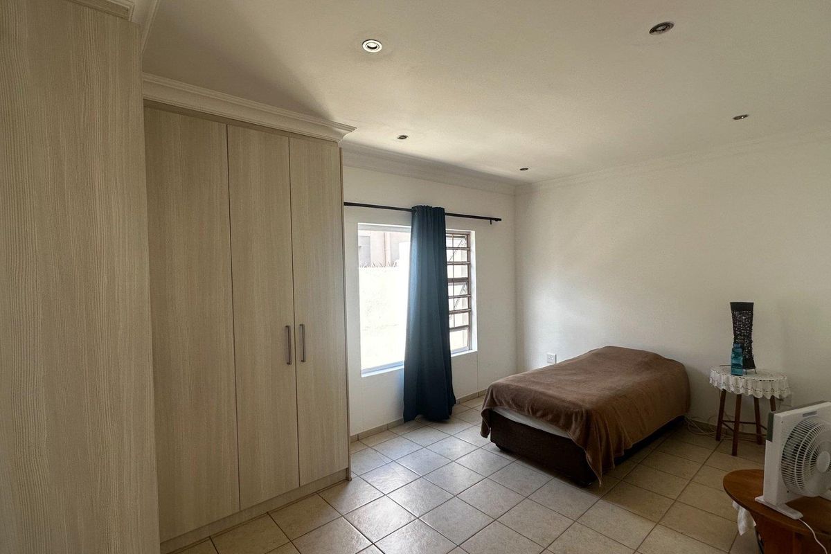 A bedroom featuring neutral floor tiles, built-in wooden cupboards, and recessed ceiling lighting.