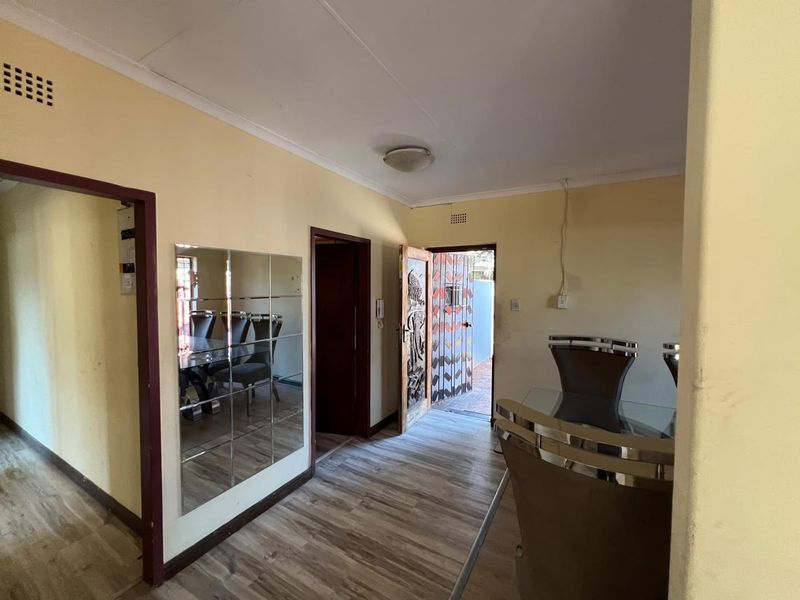 A living area featuring laminate flooring, coving, and a wall-mounted mirror, with direct access to an exterior entrance.