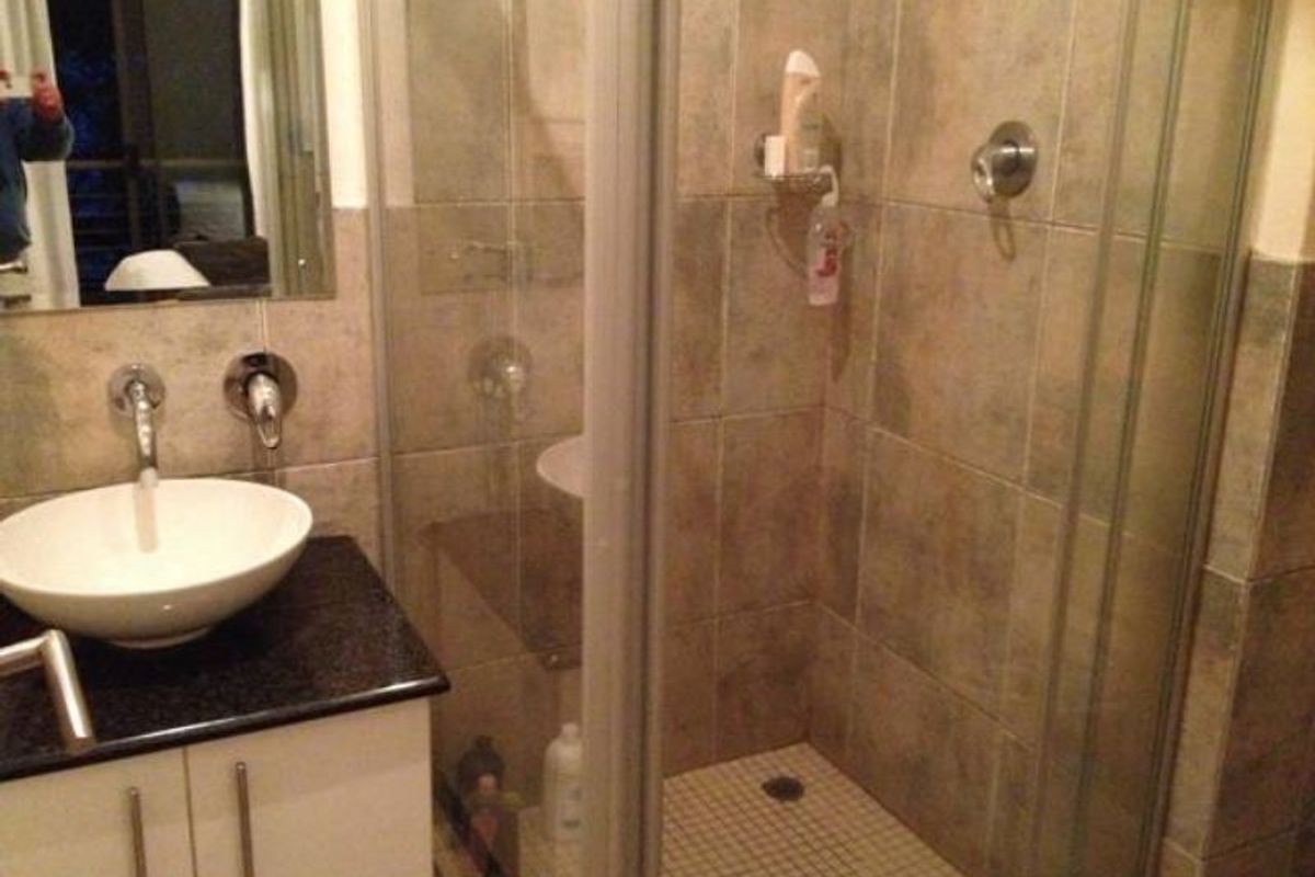 A compact bathroom featuring a modern vessel sink on a granite vanity, paired with a glass-enclosed shower and neutral wall tiling.
