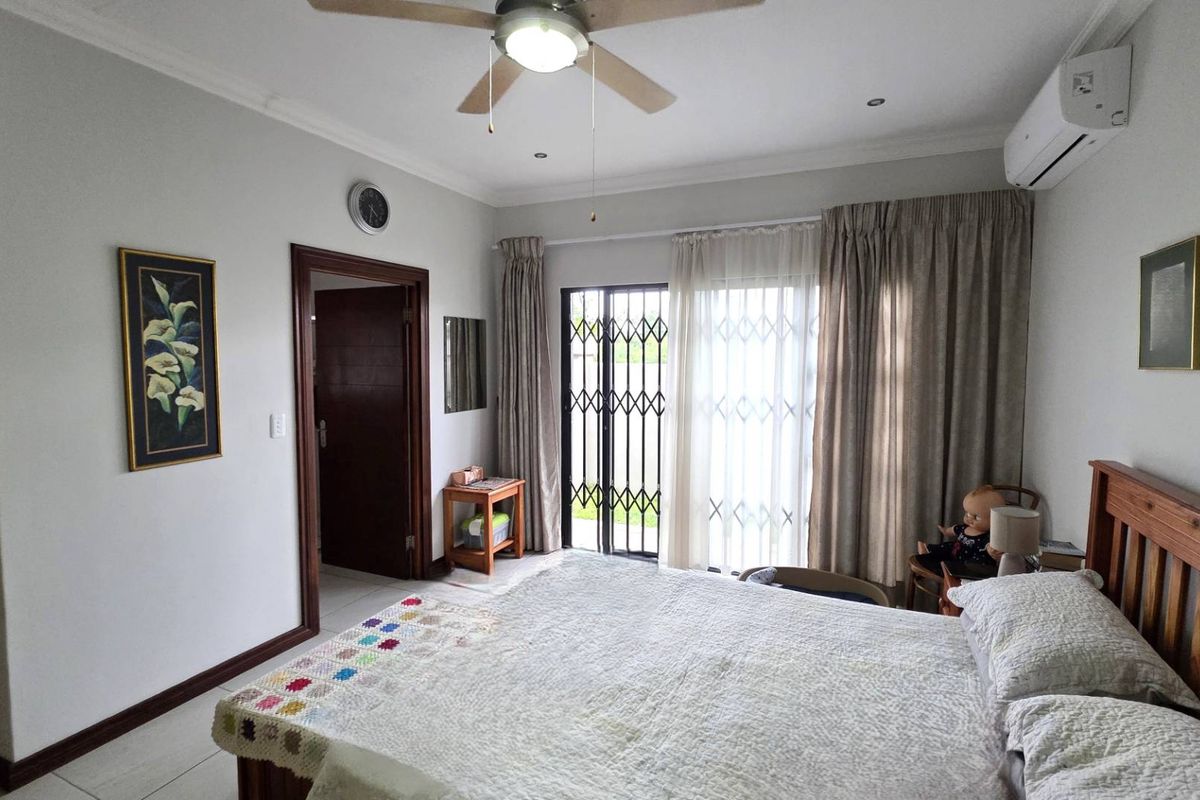 A well-lit bedroom featuring tiled flooring, a ceiling fan, a split-system air conditioner, and a sliding glass door with a security gate.