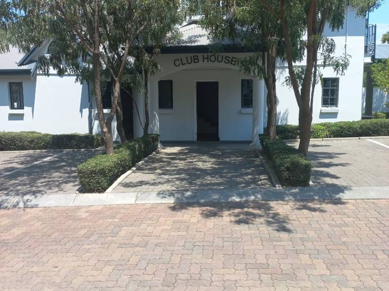 Exterior view of the apartment complex clubhouse featuring a paved driveway, mature trees, and landscaped hedges leading to the main entrance.