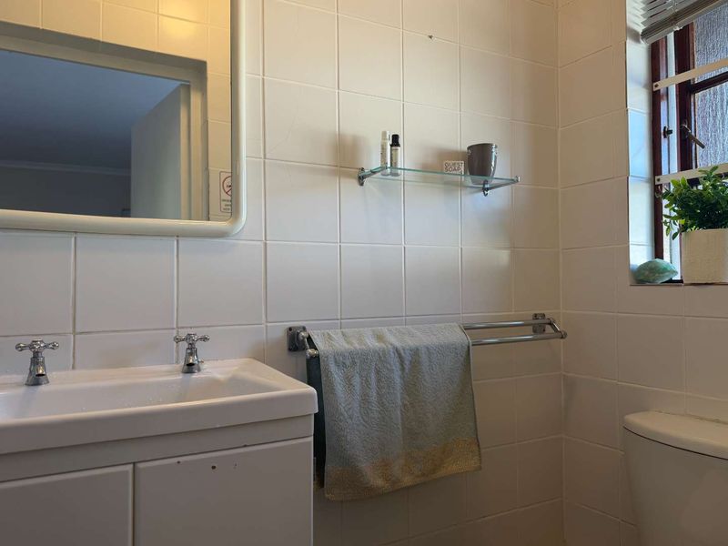 A functional bathroom featuring a vanity basin, wall-mounted mirror, glass shelving, and classic white ceramic wall tiling.