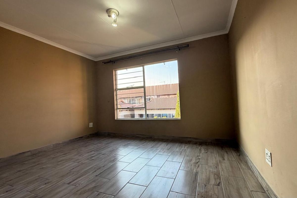 An empty bedroom featuring wood-look tiled flooring, a window with security bars, and neutral wall paint, ready for personalization.