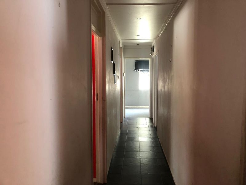 A narrow residential hallway featuring dark tiled flooring and recessed ceiling lighting, leading towards an adjacent room.
