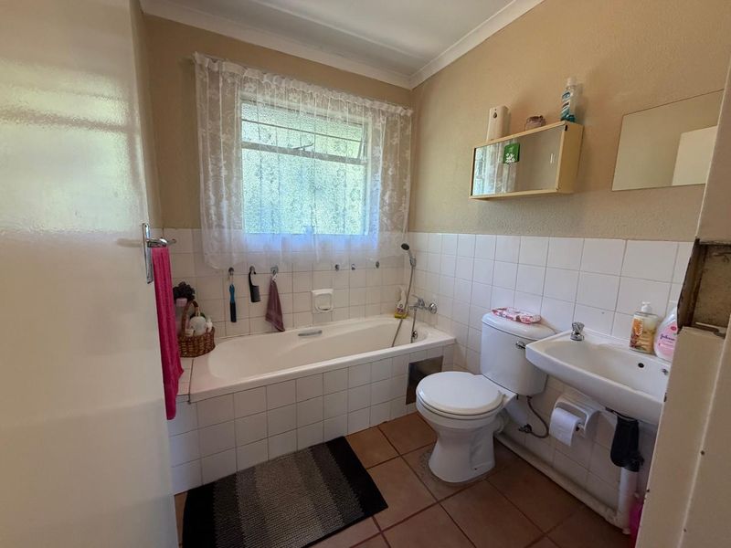 A functional bathroom featuring a bathtub, pedestal basin, and toilet, with tiled finishes and a wall-mounted cabinet, requiring cosmetic updates.