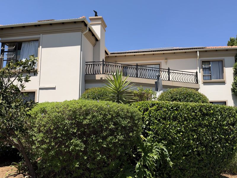 Rear elevation of a two-story house featuring a balcony with wrought iron railing, established garden landscaping, and a chimney stack.