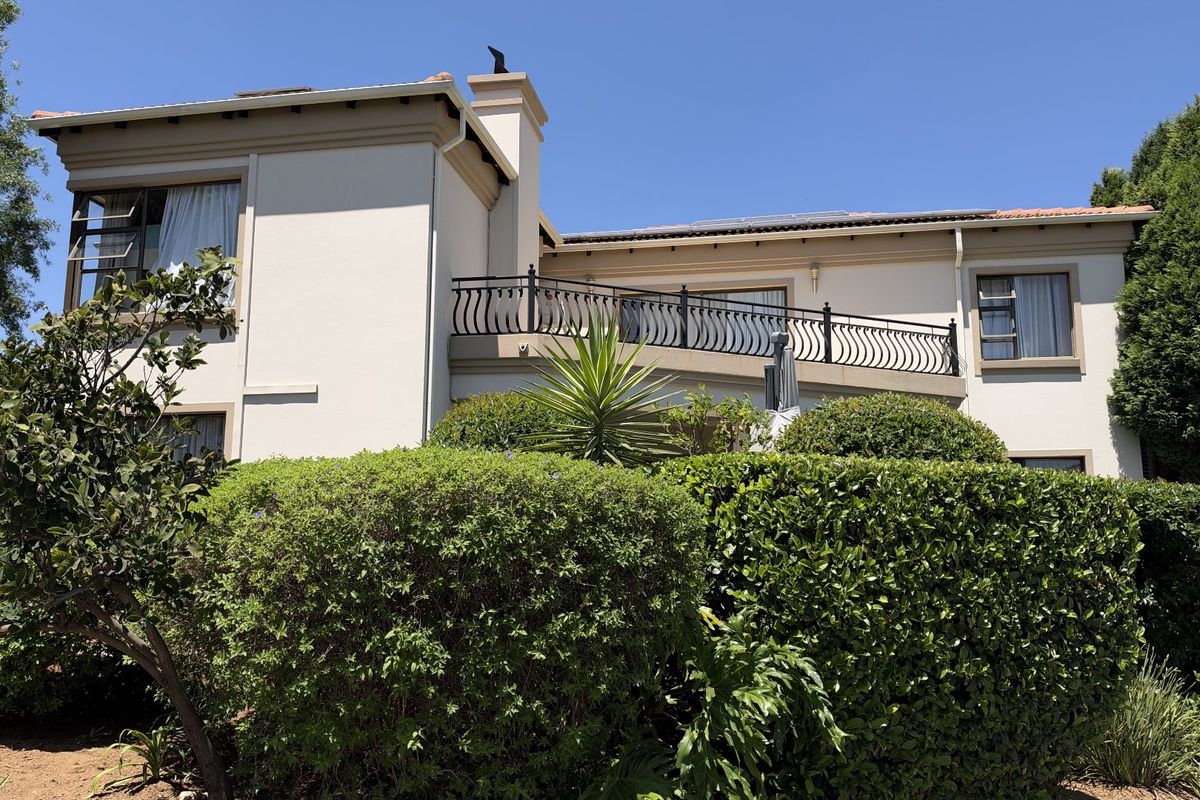 Rear elevation of a two-story house featuring a balcony with wrought iron railing, established garden landscaping, and a chimney stack.