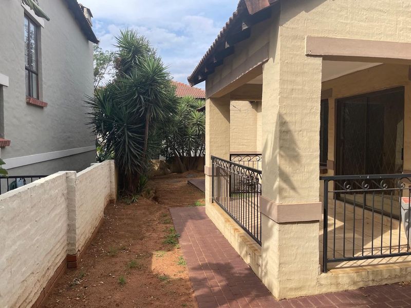 Rear exterior view featuring a covered patio with wrought iron railings, brick paving, and a side garden area.