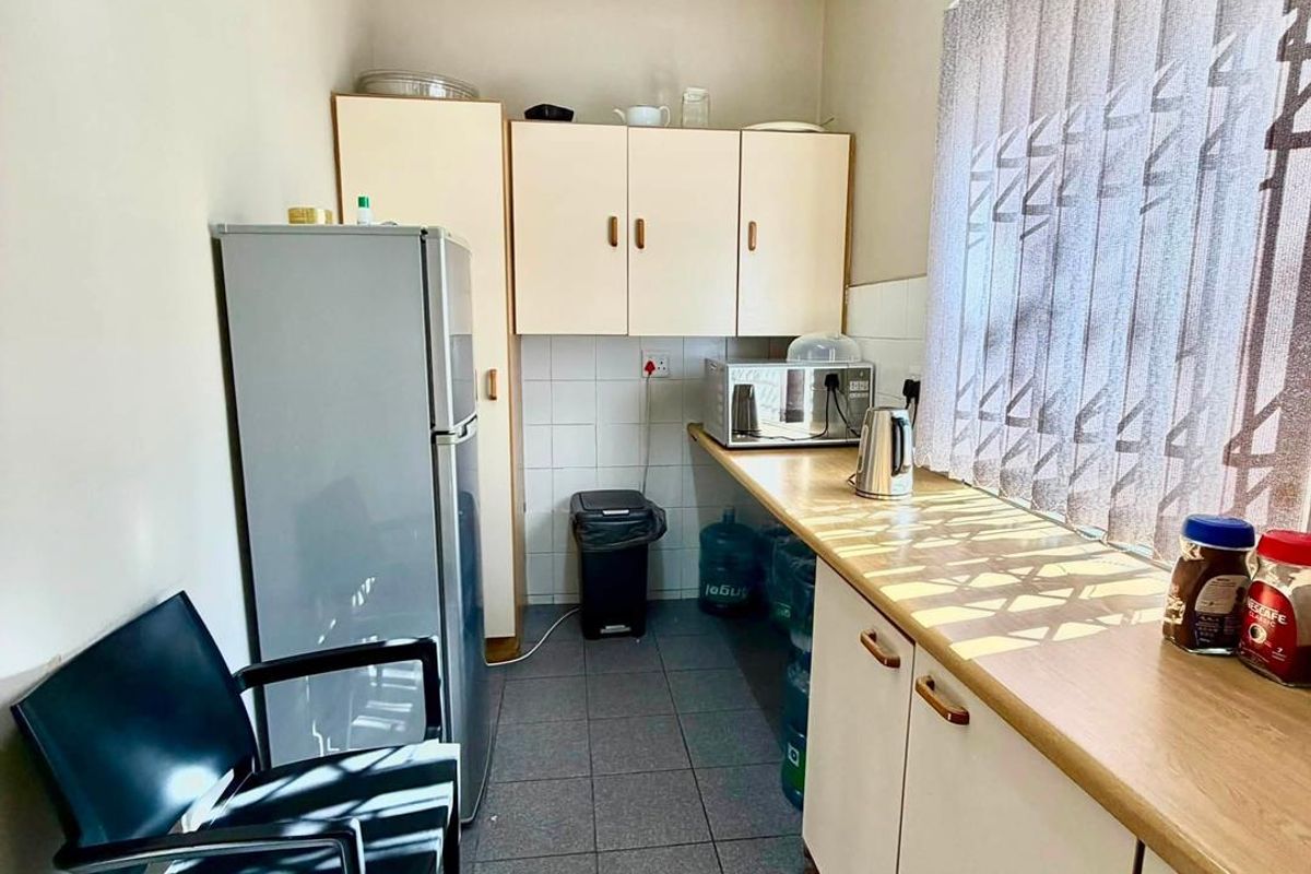 A functional kitchenette featuring built-in cabinetry, laminate countertops, tiled backsplash, and tiled flooring, providing a practical space for office refreshments.