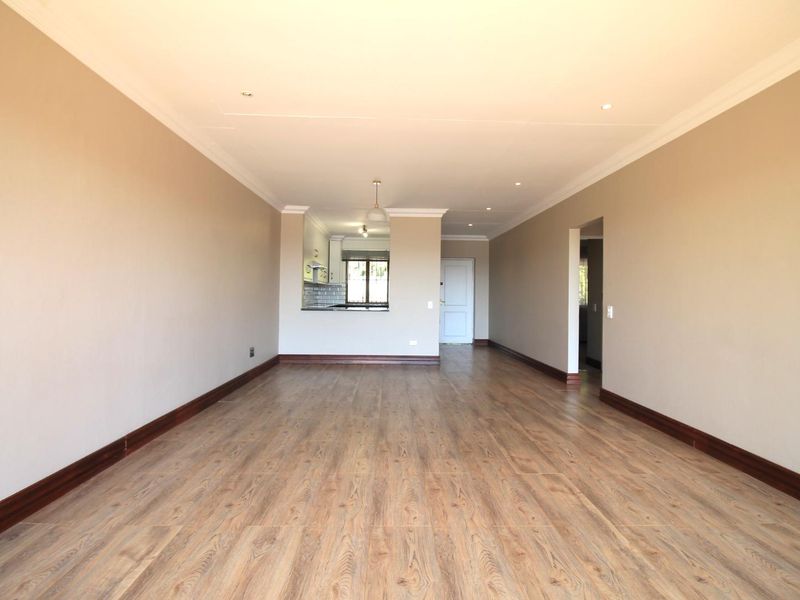 Spacious open-plan living area featuring modern laminate flooring, recessed lighting, and coved cornicing, with a clear view through to the kitchen area.