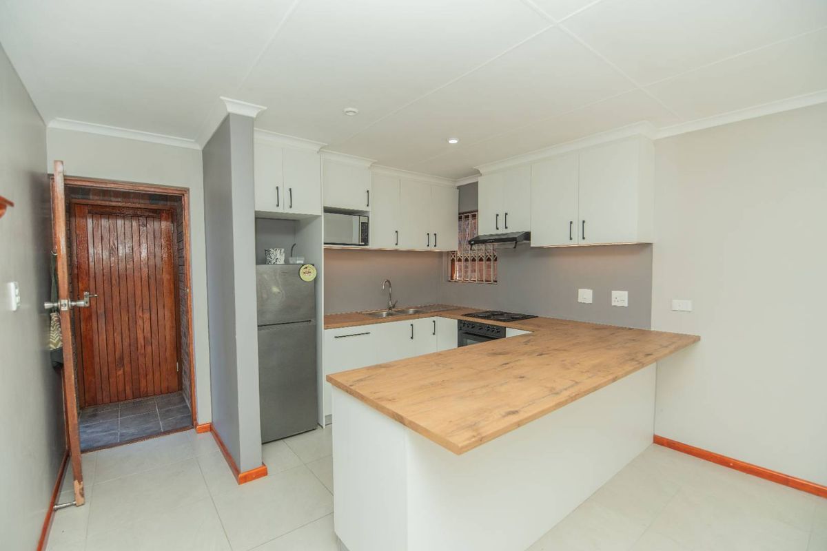Modern kitchen featuring white cabinetry, wood-look countertops, built-in oven, extractor fan, and a breakfast bar, adjacent to a wooden door entrance.