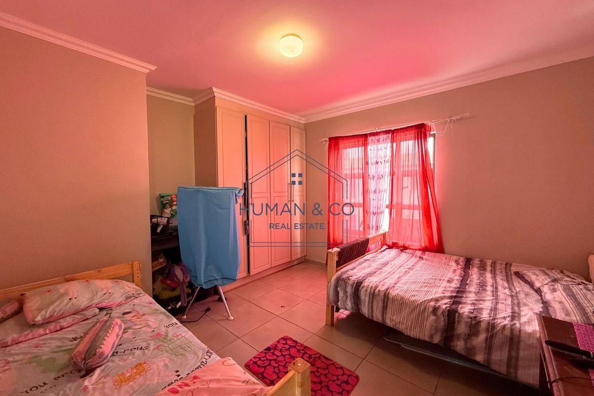 A bedroom featuring tiled flooring, built-in cupboards, and a window with red curtains, providing a functional living space.
