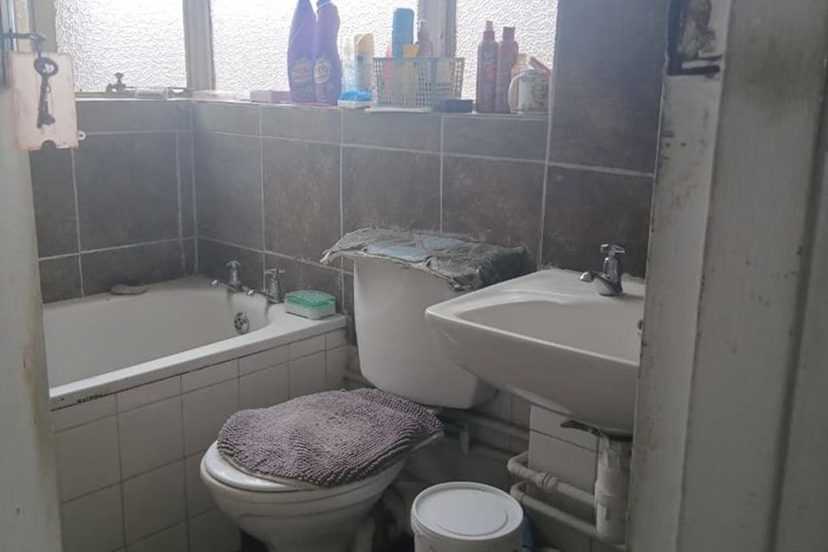 Compact bathroom featuring a standard bathtub, pedestal sink, and toilet with dated wall tiling and visible plumbing fixtures.