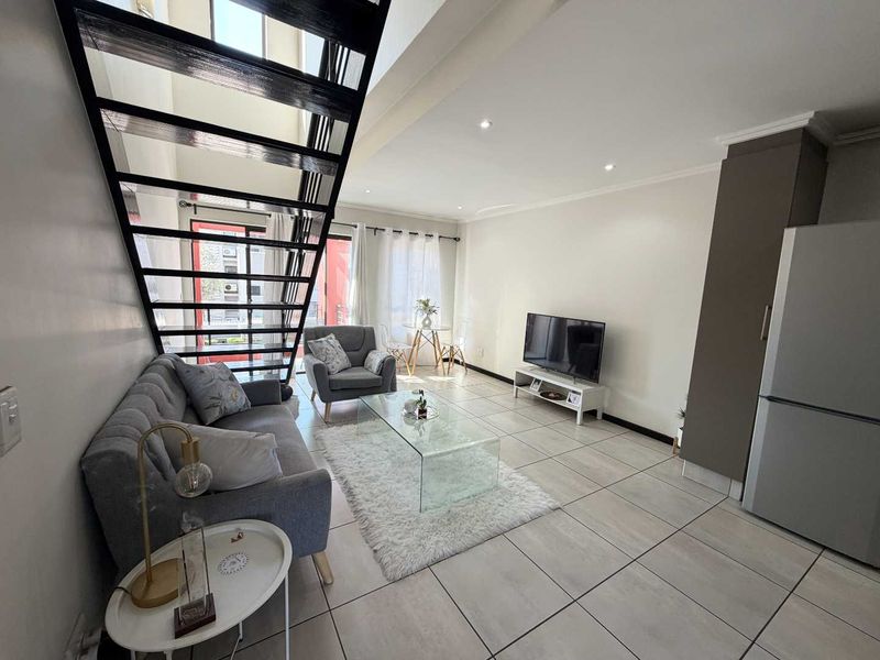 Open-plan living area featuring modern tiled flooring, a striking staircase, and access to a balcony through a sliding door.