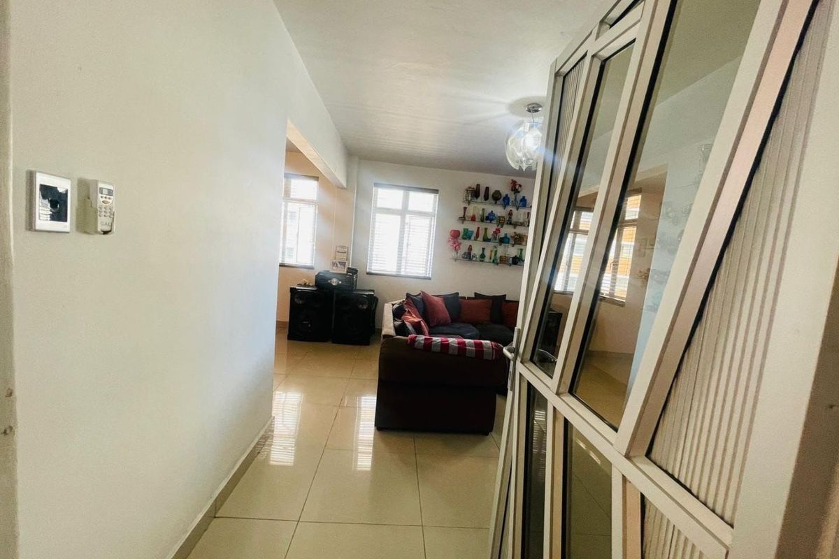 A view from the hallway into a living area featuring tiled flooring and an aluminium framed glass door.