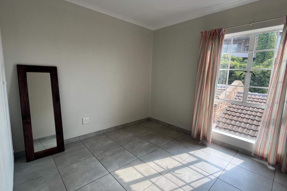 A bright, empty bedroom featuring neutral walls, tiled flooring, and a window with security bars, offering a clean canvas for personalization.