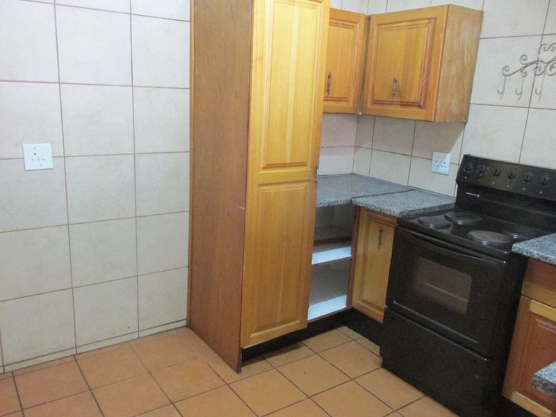 A functional kitchen featuring wooden cabinetry, granite countertops, and a freestanding electric stove, finished with ceramic wall and floor tiles.