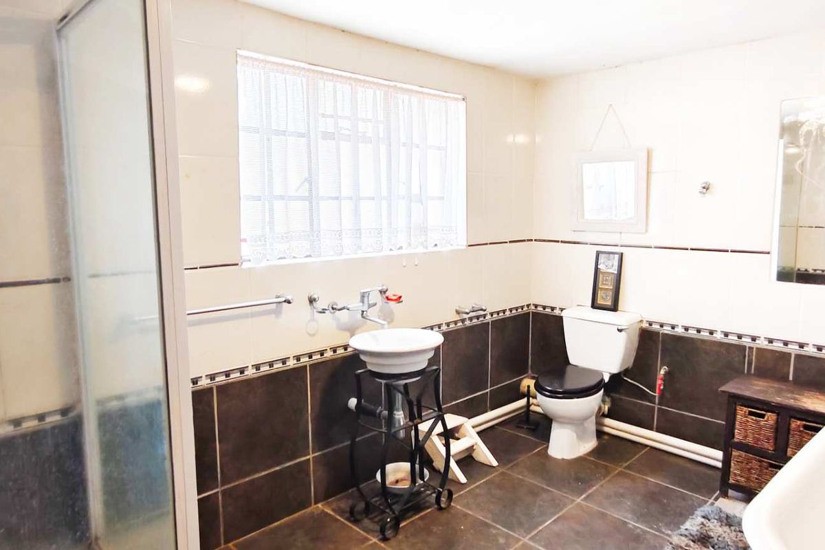 A functional bathroom featuring a shower enclosure, pedestal basin, and toilet with contrasting dark floor and wall tiles.